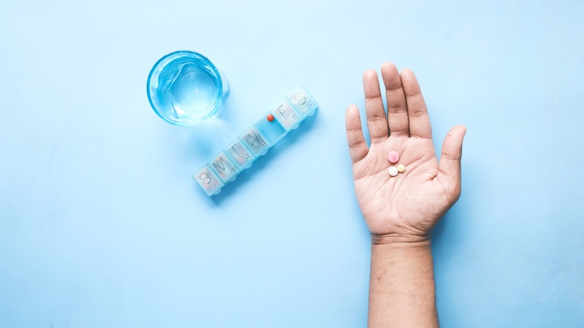 top view of pills on palm of hand with pill box and glass on water on table